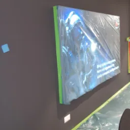 Świeżo pomalowana, grafitowa ściana zabezpieczona folią malarską z obrazem w ramie również owiniętym folią ochronną.