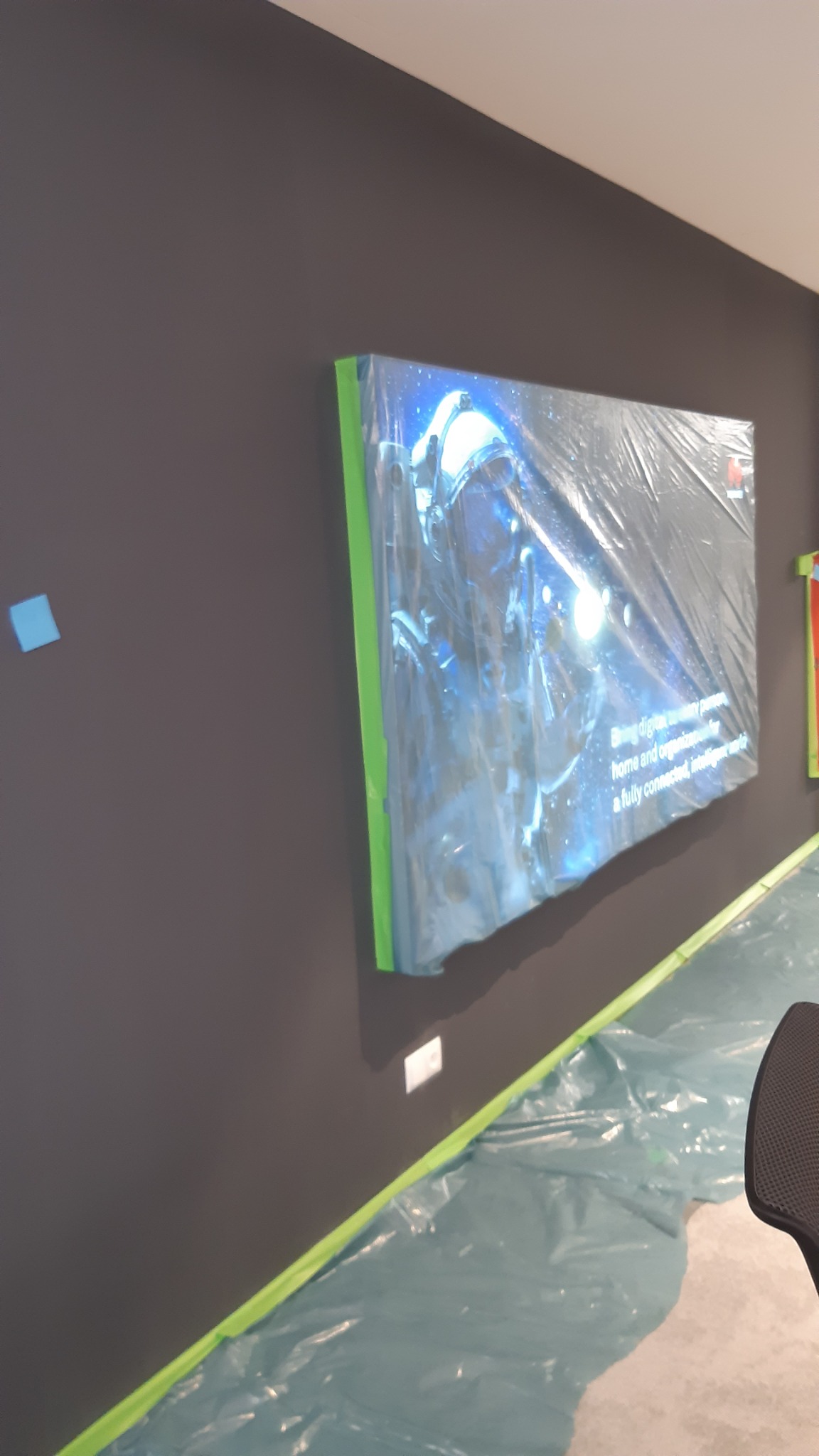 Świeżo pomalowana, grafitowa ściana zabezpieczona folią malarską z obrazem w ramie również owiniętym folią ochronną.