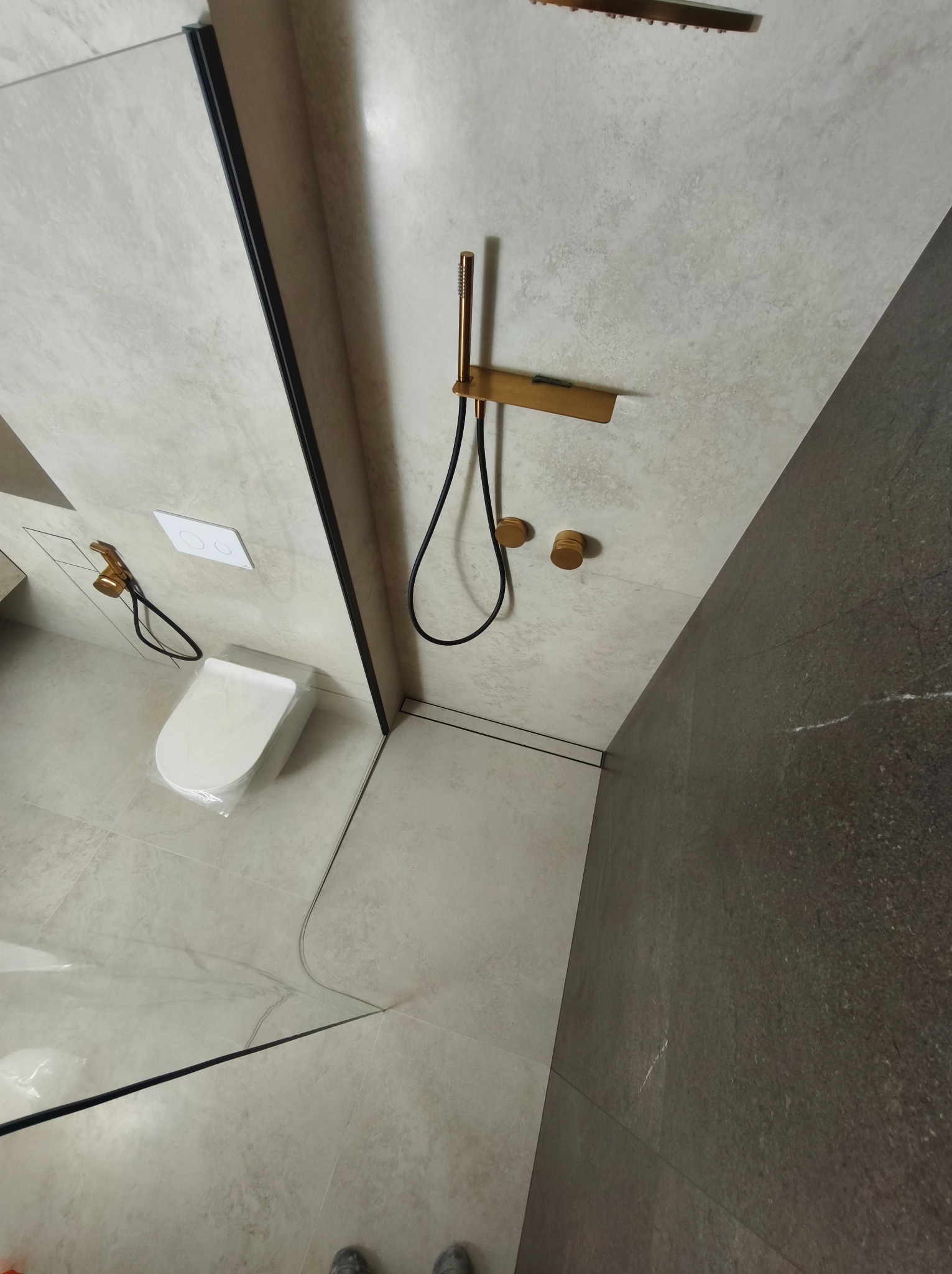 Nowoczesna kabina prysznicowa z elementami w kolorze złotym, widok z góry. Uwagę zwracają szare płytki i minimalistyczny design.