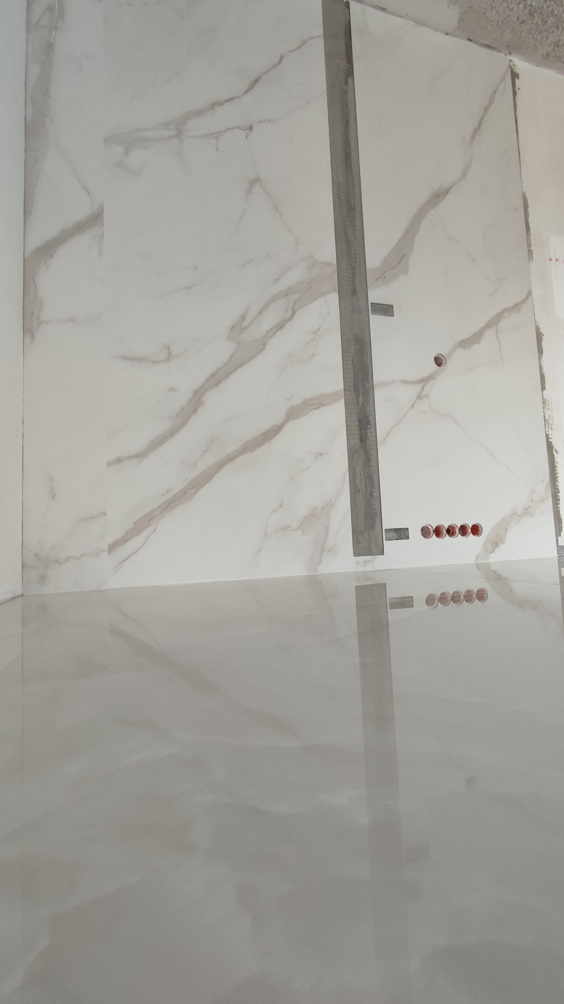 Połyskująca posadzka i ściana wyłożona płytami imitującymi marmur, z widoczną listwą montażową i otworami na gniazdka.