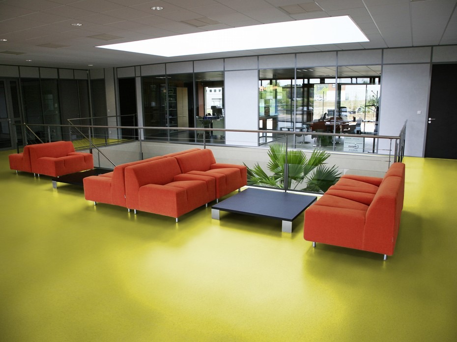 Jasnożółta podłoga z wykładziny PVC w nowoczesnym biurze z pomarańczowymi sofami i palmą w tle