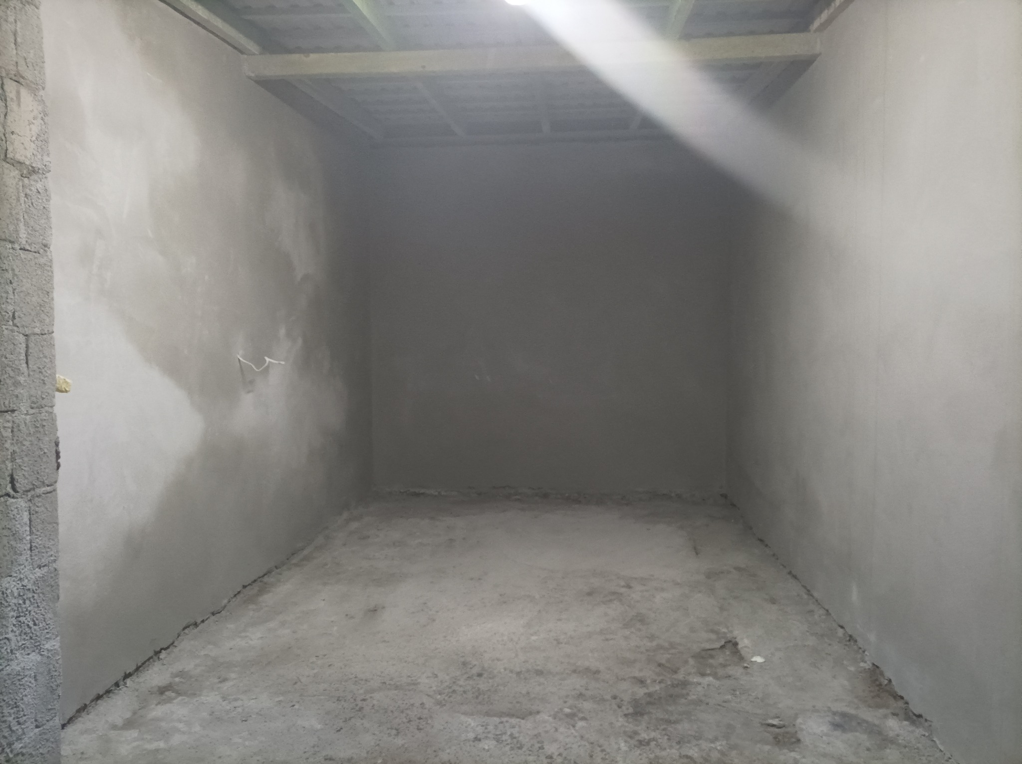 Wnętrze pomieszczenia po nałożeniu szarego tynku, widoczne ślady po instalacji elektrycznej na ścianie, surowe wykończenie podłogi i brak listew przypodłogowych.