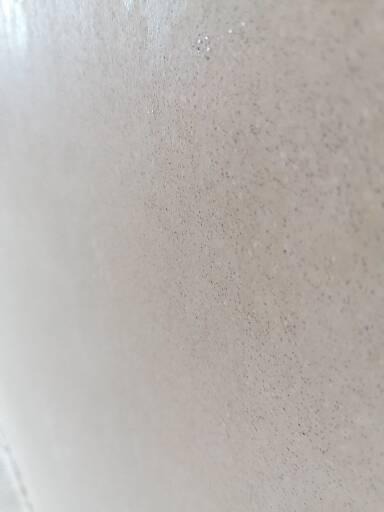 Świeżo nałożony, jasny tynk z delikatną fakturą, widoczne drobne nierówności i delikatny połysk pod światło.