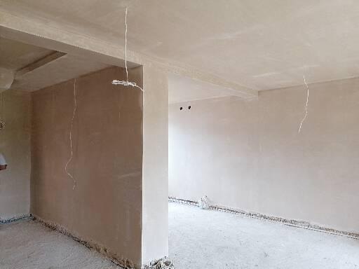 Wnętrze po nałożeniu gładzi gipsowej, widoczne przewody elektryczne wystające ze ścian i sufitu, surowy stan wykończenia.