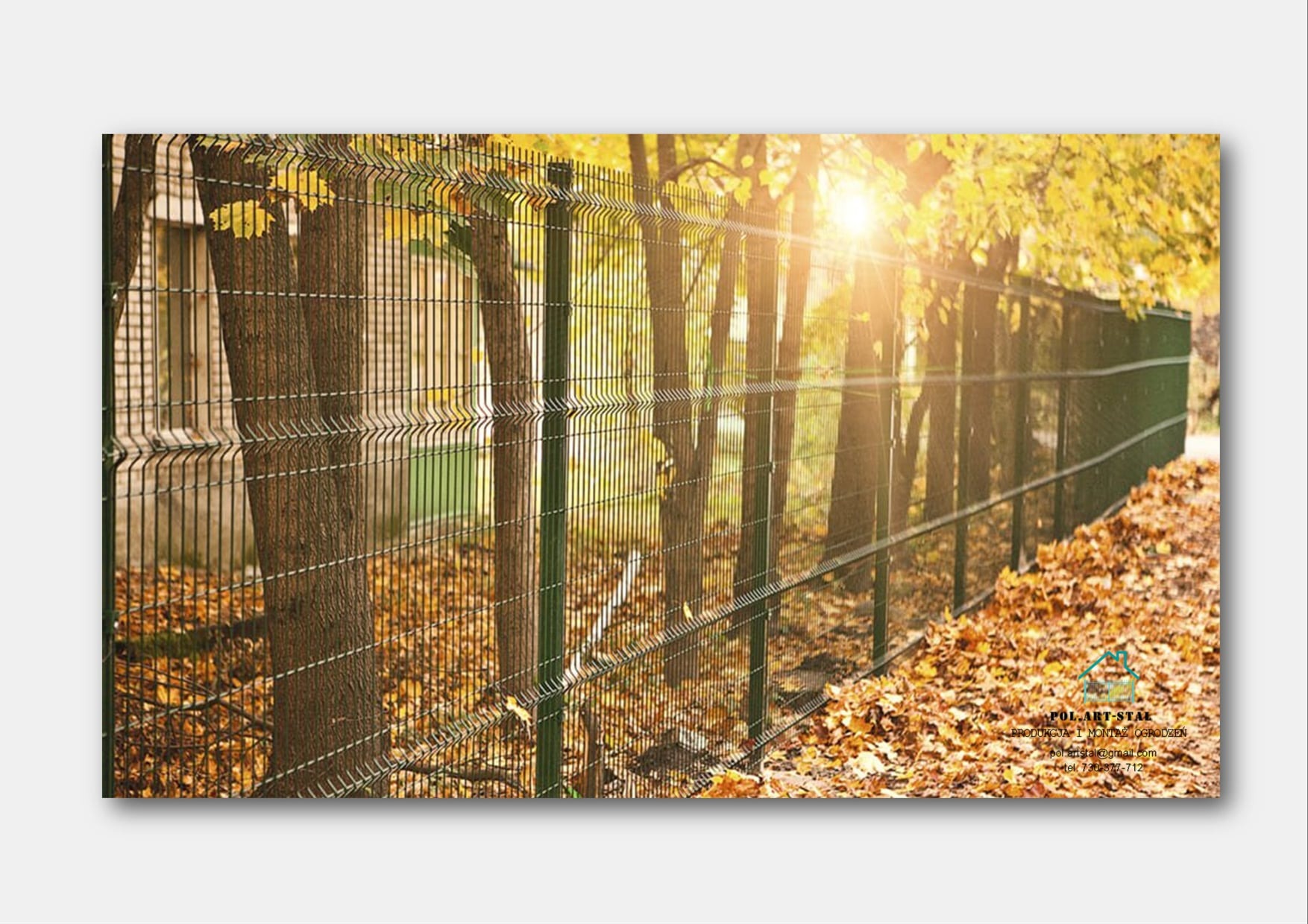 Zielone panele ogrodzeniowe z siatki zgrzewanej, zamontowane na tle jesiennych drzew i opadłych liści, oświetlone promieniami słońca.