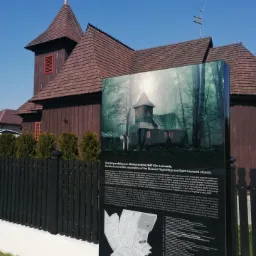 Tablica informacyjna z nadrukiem UV przedstawiająca Kościół parafialny pw. Wniebowzięcia NMP i Św. Leonarda na tle rzeczywistego kościoła w tle.