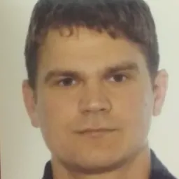 Portret mężczyzny z krótkimi ciemnymi włosami, skierowany en face, na jasnym tle.