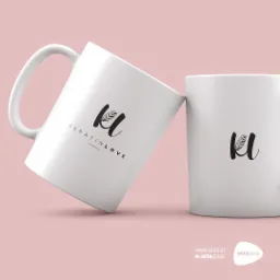 Dwie białe ceramiczne filiżanki z czarnym logo 'KL Keratin Love Hair Spa' ustawione na jasnoróżowym tle, z widocznym adresem strony internetowej w prawym dolnym rogu.