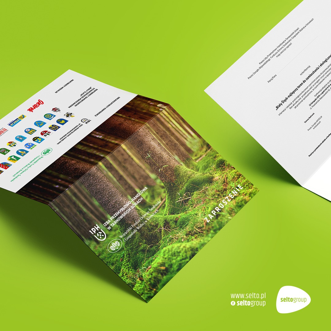 Rozłożona broszura zapraszająca na konferencję o ekologii, z motywem lasu i mchu, leżąca na zielonym tle obok białej kartki z tekstem.