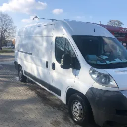 Biały samochód dostawczy Fiat Ducato po umyciu na kostce brukowej przed myjnią samochodową z akcesoriami na dachu.