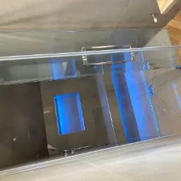 Nowoczesna kabina prysznicowa z grafitowymi płytkami, wnęką podświetloną na niebiesko i odpływami liniowymi, połączona z podłogą wyłożoną parkietem w jodełkę.