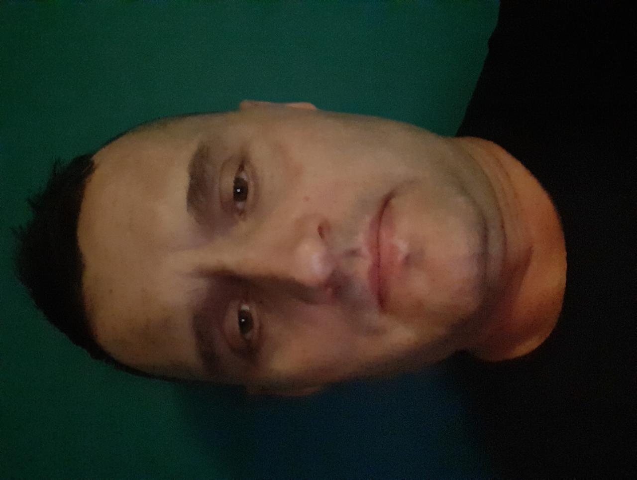 Portret mężczyzny z krótkimi włosami, skierowany w lewo, na zielonym tle. Widoczne rysy twarzy, skupiony wzrok. Obrócone ujęcie.