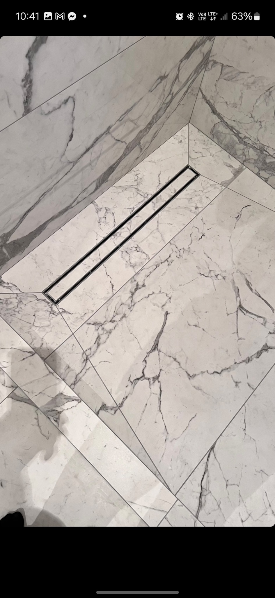 Wykończona łazienka z marmurowymi płytkami i liniowym odpływem podłogowym.