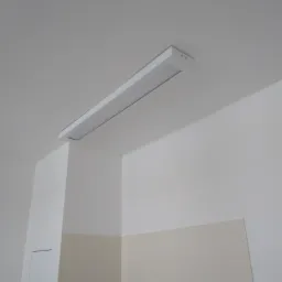 Nowoczesna, długa lampa LED zamontowana na suficie w rogu pomieszczenia z białymi ścianami i częściowo wyłożonymi jasnymi płytkami.