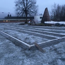 Bruk-Majstero - Przygotowany teren pod budowę tarasu, z obramowaniem z kostki, widoczne pręty zbrojeniowe i elementy konstrukcyjne w tle, pochmurny dzień.