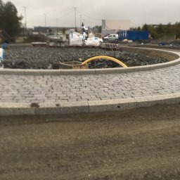 Bruk-Majstero - Obrzeże z kostki granitowej ułożone w okrąg, widoczne materiały budowlane i żółty wąż na placu budowy w pochmurny dzień.