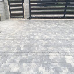 Bruk-Majstero - Nowoczesna, pozioma brama wjazdowa z szarymi, betonowymi słupkami i podjazdem wyłożonym szarą kostką o nieregularnym kształcie, widok z góry.