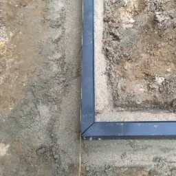 Przygotowanie podłoża pod nawierzchnię z obrzeżami, widoczna żółta linka wyznaczająca linię, ziemia częściowo wyrównana.