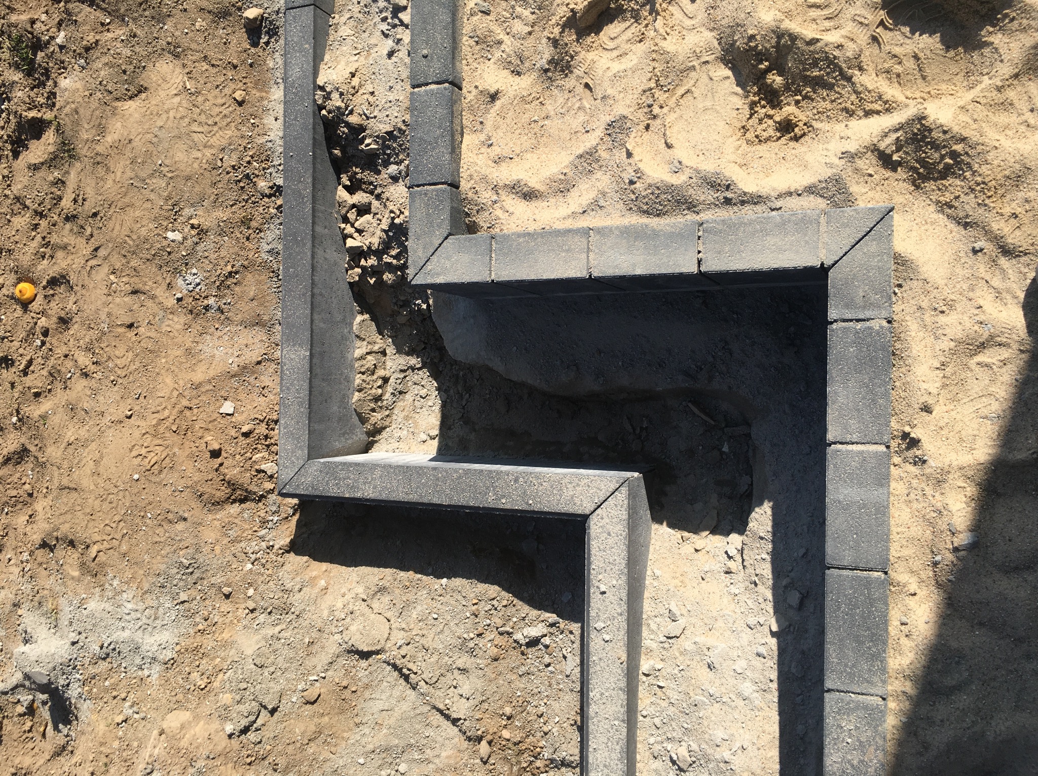 Fragment obrzeża z szarej kostki granitowej, ułożonego w ziemi, widoczne ślady stóp i samotna żółta kulka.