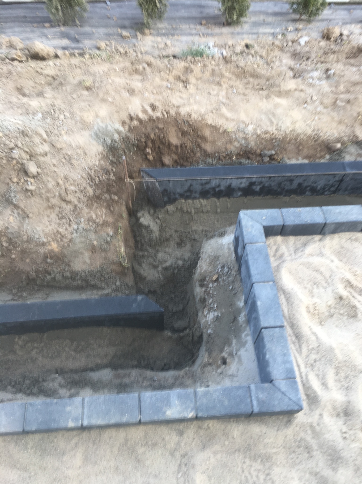 Przygotowanie podłoża pod taras: wykop z widocznymi krawężnikami i obrzeżami z kostki betonowej, częściowo wypełniony piaskiem.