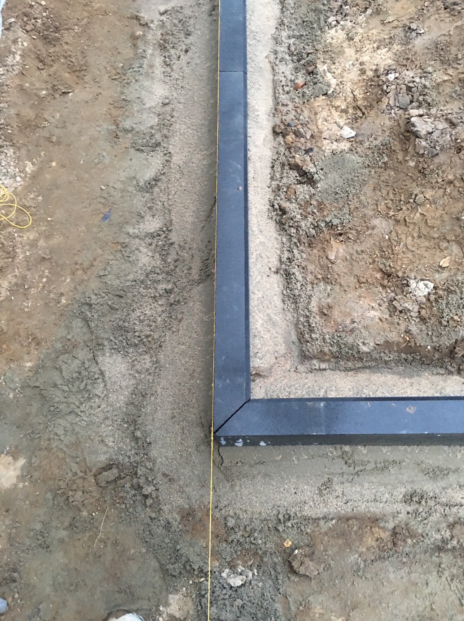 Przygotowanie podłoża pod nawierzchnię z obrzeżami, widoczna żółta linka wyznaczająca linię, ziemia częściowo wyrównana.