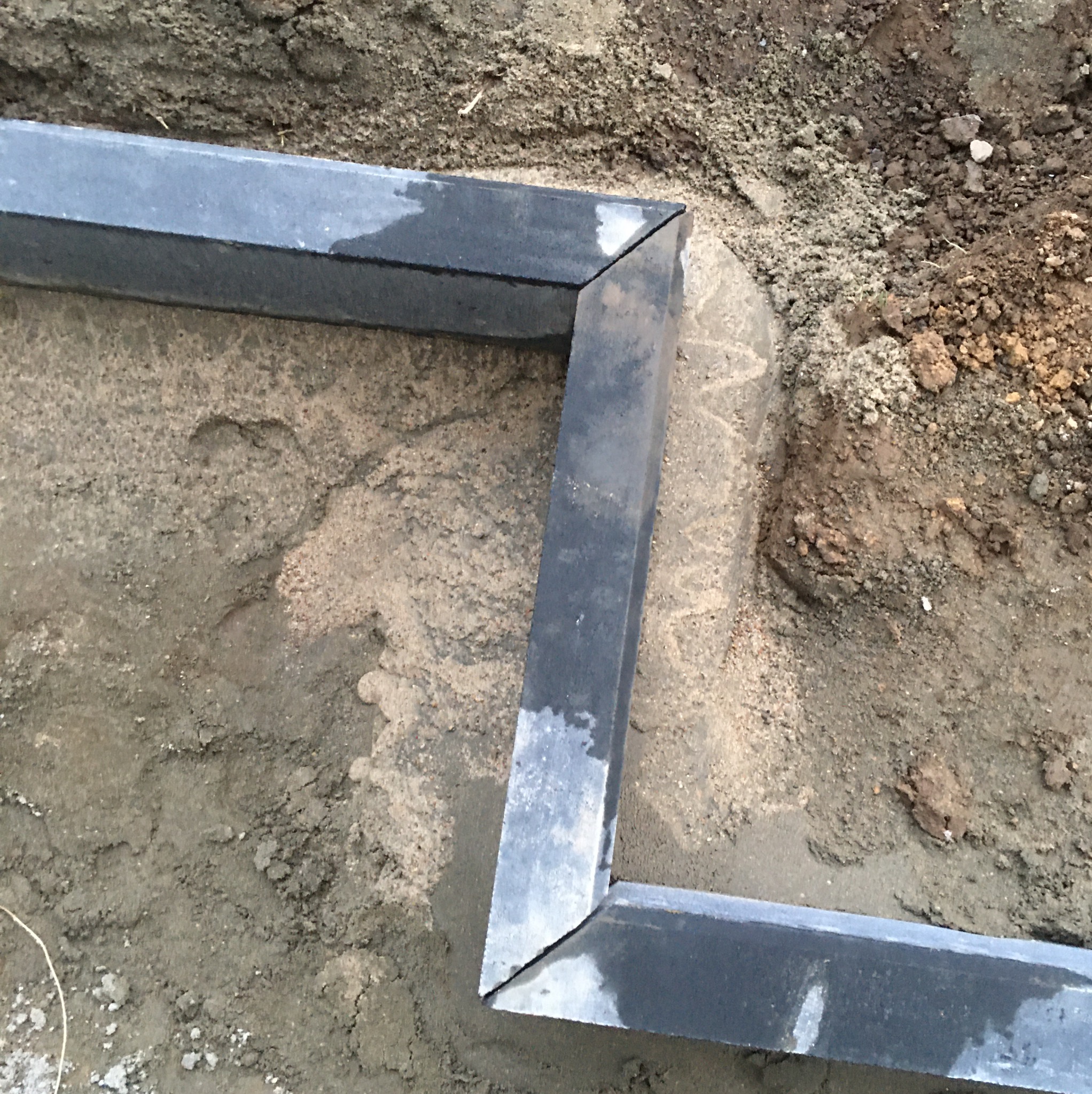 Przygotowany wykop z osadzonym obramowaniem z szarej kostki granitowej, widoczny piasek i ziemia.