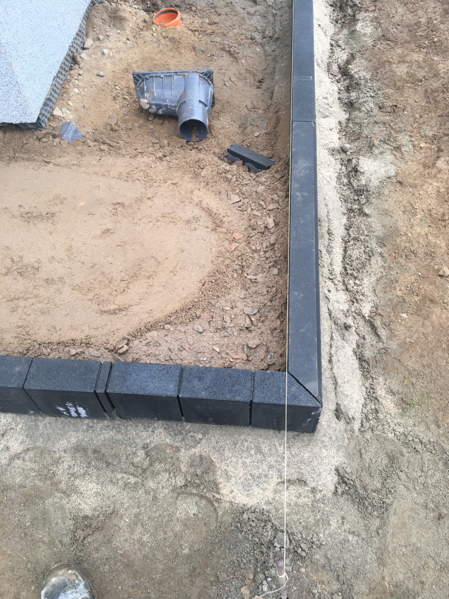 Wykop pod obrzeża z czarnej kostki brukowej, widoczny drenaż liniowy i przygotowane podłoże pod kostkę.