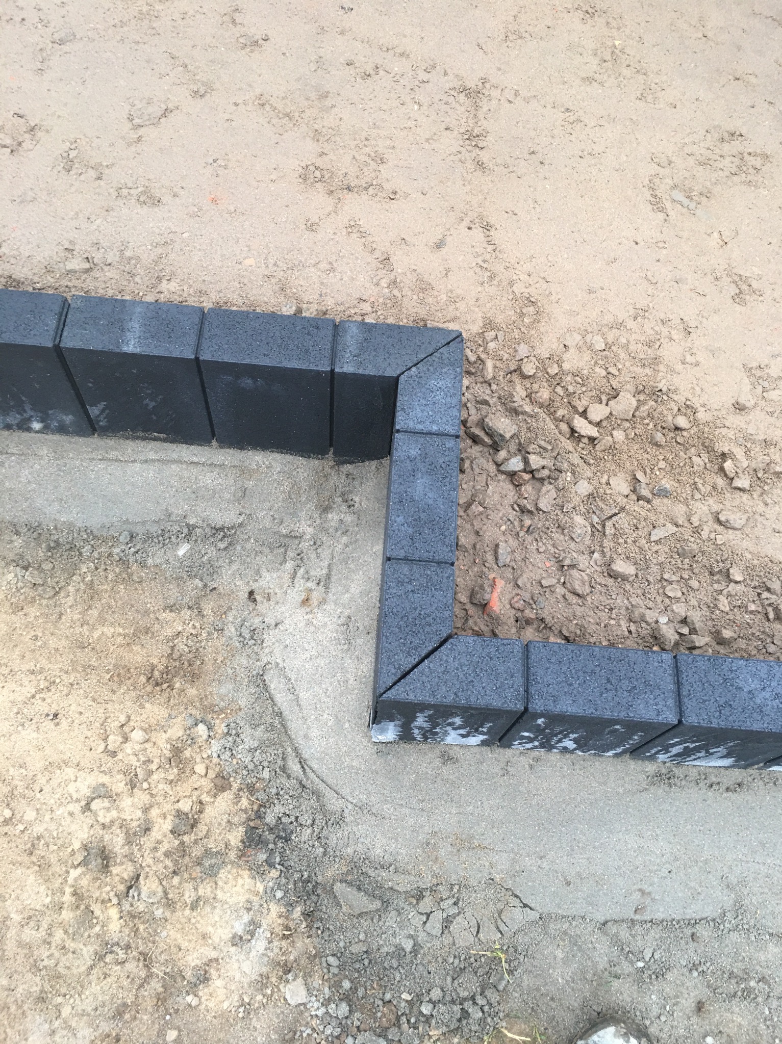 Fragment układanej nawierzchni z ciemnoszarej kostki brukowej, widoczne podłoże z piasku i zaprawy, etap prac przygotowawczych.