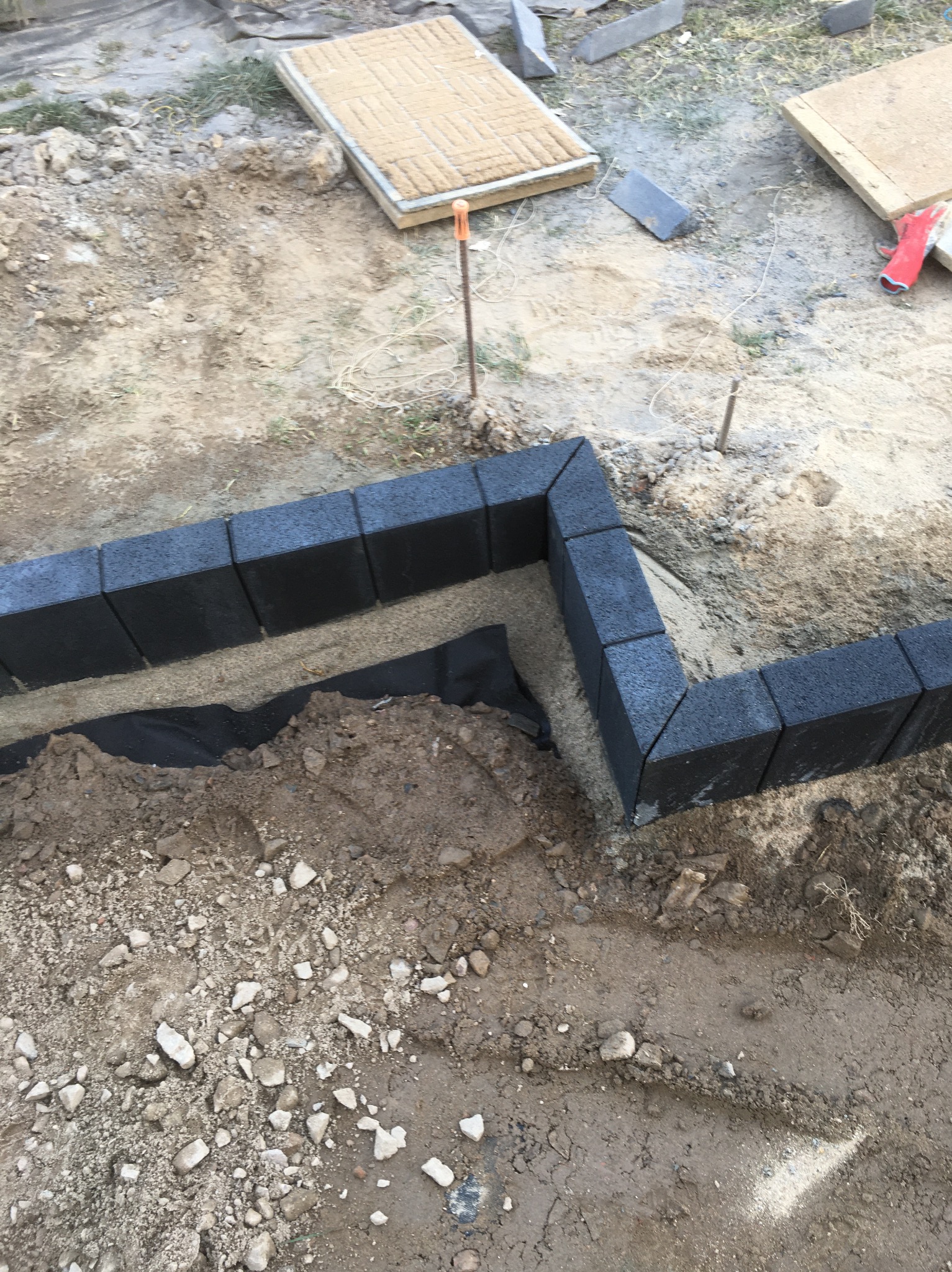Częściowo ułożona obwódka z czarnej kostki brukowej na podsypce piaskowej z geowłókniną, widoczne przygotowane podłoże i kostka w tle.