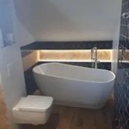 Wykończona łazienka w Tarnowskich Górach z wolnostojącą wanną, podwieszaną toaletą i podświetlaną półką pod skosem dachu.