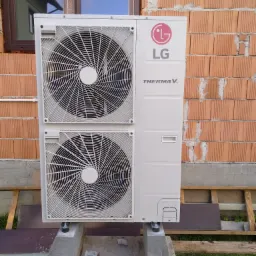 Zewnętrzna jednostka pompy ciepła LG Therma V zamontowana na betonowych podstawach przy ścianie z czerwonej cegły, widoczne narzędzia instalacyjne.
