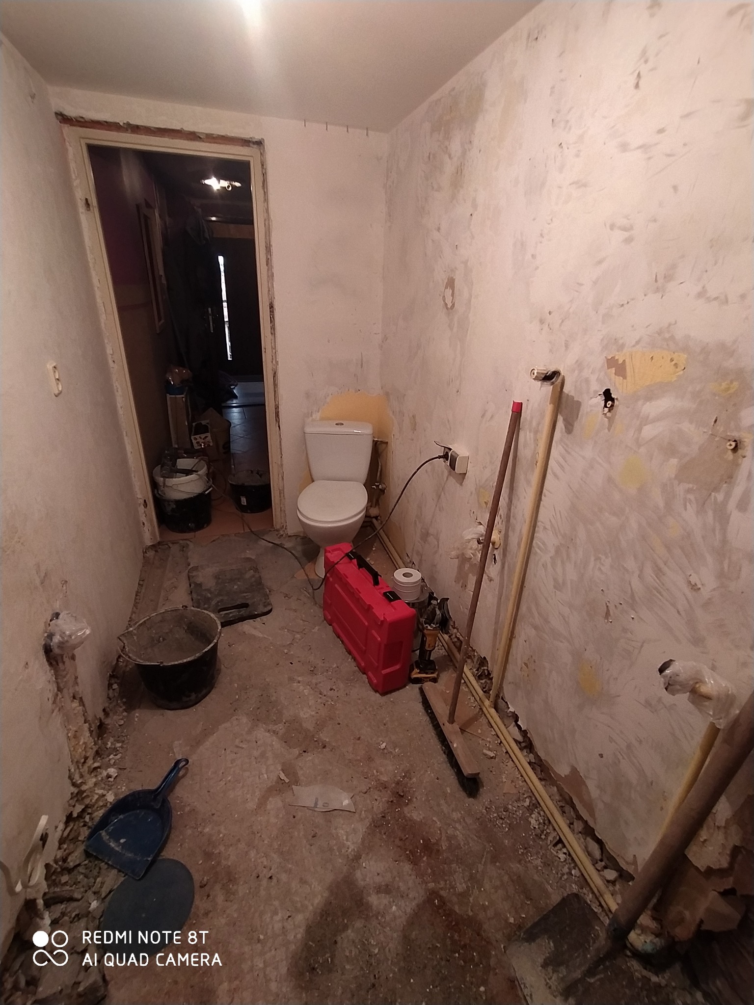 Łazienka w trakcie remontu: widoczne gołe ściany, instalacja hydrauliczna, narzędzia i toaleta z żółtą deską.