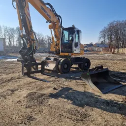 Żółto-biała koparka Liebherr z zamontowanymi widłami i łyżką na ziemnym placu budowy w słoneczny dzień.