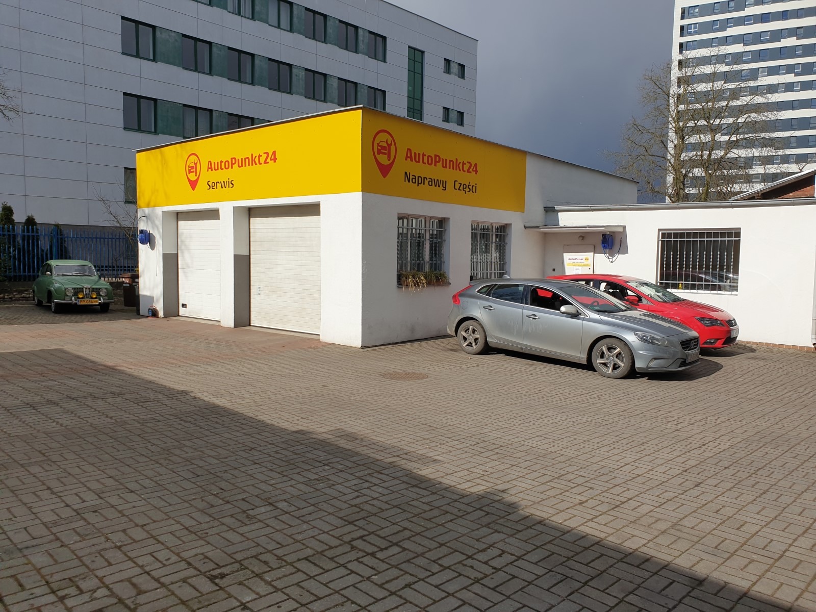 Budynek serwisu samochodowego 'AutoPunkt24' w Bydgoszczy z zaparkowanymi samochodami: srebrnym Volvo i czerwonym Seatem oraz zielonym Saabem z przodu garażu.