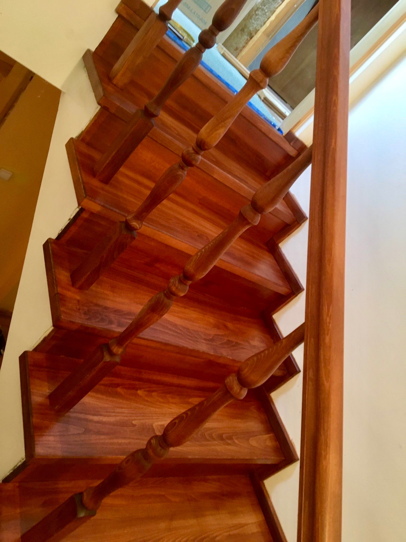 Polerowane, drewniane schody z balustradą, widziane z góry pod kątem. Ciepłe oświetlenie podkreśla rysunek drewna. Widoczne detale wykończenia.