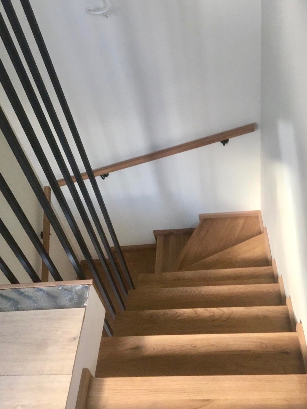 Nowoczesne schody drewniane z czarną balustradą i drewnianą poręczą, widok z góry. Jasne drewno stopni kontrastuje z ciemnymi elementami metalowymi.