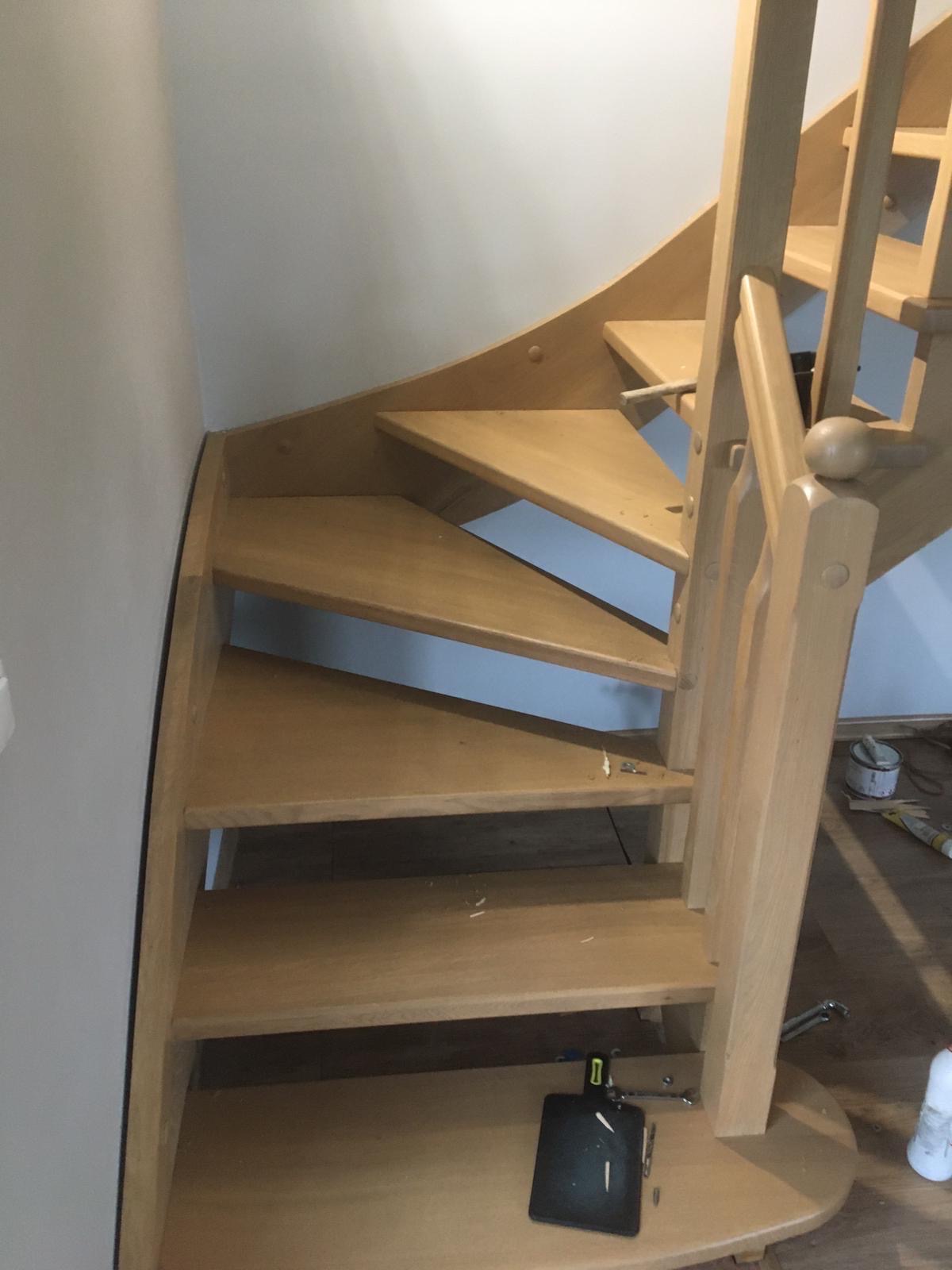 Jasne, drewniane schody kręcone w trakcie montażu, widoczne narzędzia i drobne wióry. Ujęcie z dołu, podkreślające konstrukcję i etap prac wykończeniowych.