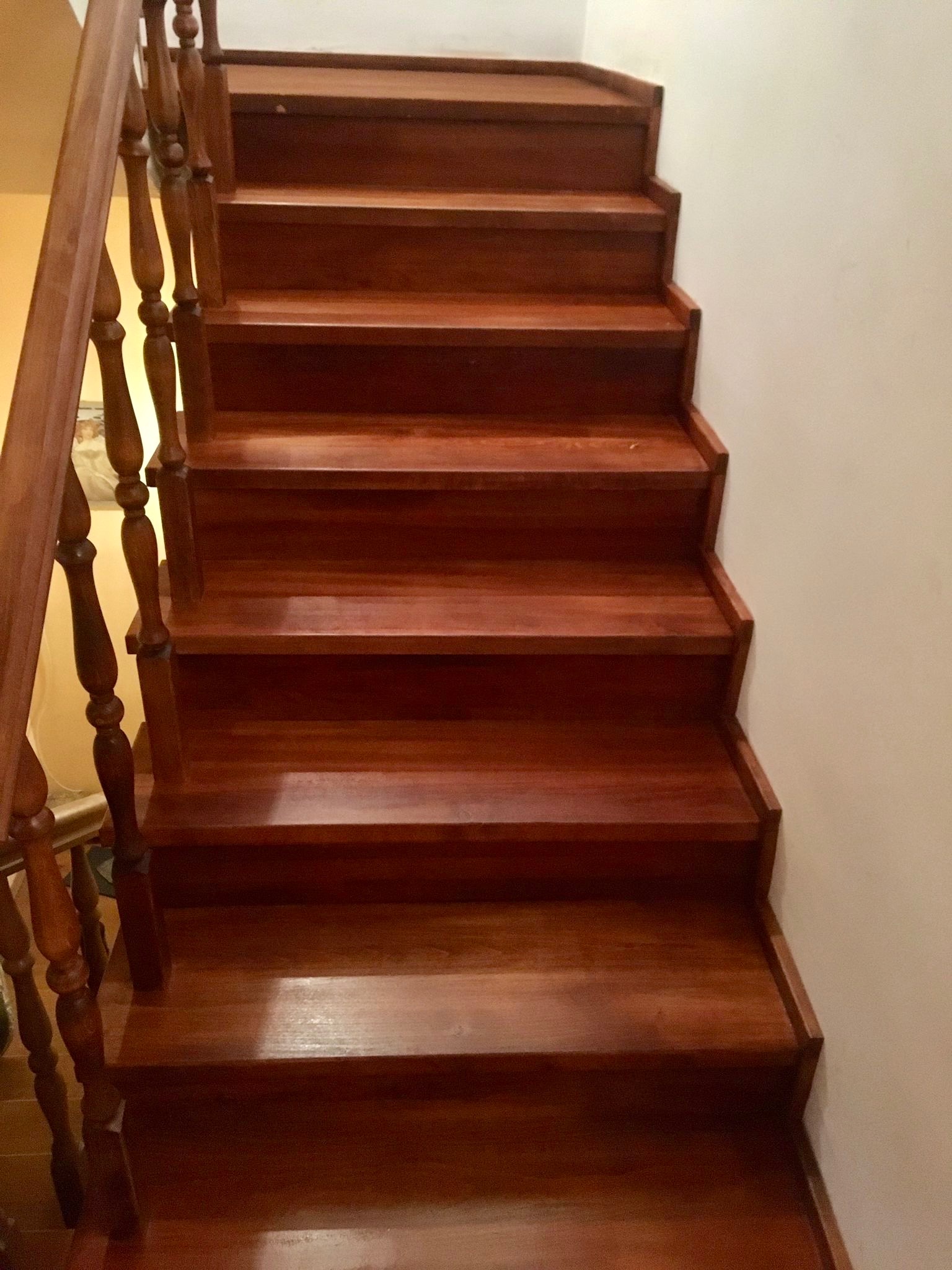 Polerowane, drewniane schody w odcieniach brązu z ozdobną balustradą, widoczne z dołu, oświetlone ciepłym światłem.