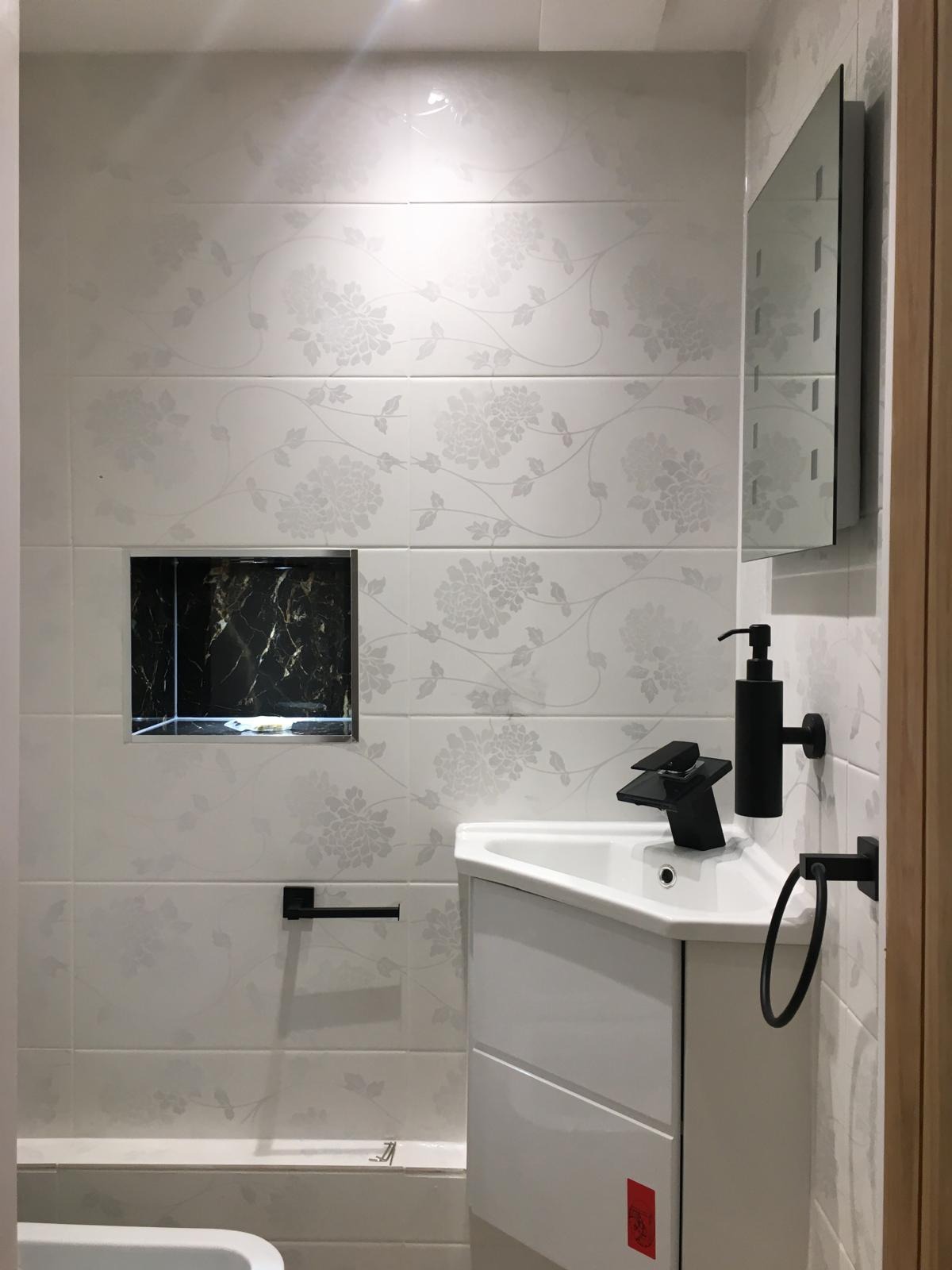 Nowoczesna łazienka z białymi płytkami w kwiaty, czarną armaturą i wnęką z czarnym marmurem.