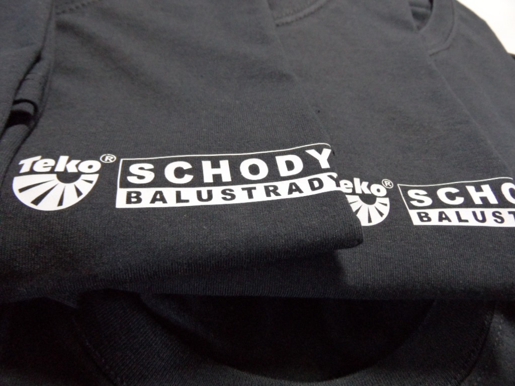 Ciemnoszara koszulka z białym nadrukiem logo firmy 'SCHODY BALUSTRADY Teko' z Wielkiej Wsi, złożona w stos.