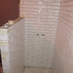 Świeżo ułożone, błyszczące, białe płytki w kształcie cegiełek na ścianach prysznica, z widocznymi krzyżykami dystansowymi i śladami fugi, przygotowane do dalszych prac wykończeniowych.