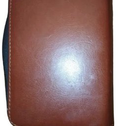 Adrian Gonet - Zamknięty, brązowy, skórzany organizer z czarnym zamkiem błyskawicznym i uchwytem.