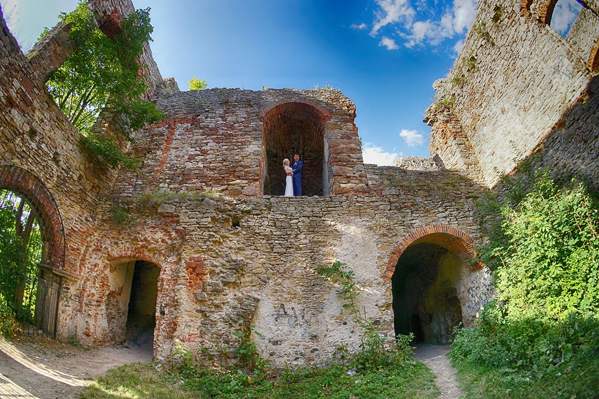 Para młoda w objęciach na tle ruin zamku z cegły i kamienia, malowniczy krajobraz i błękitne niebo.