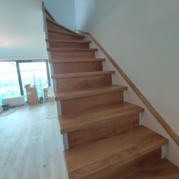 Drew-klas - Nowoczesne schody drewniane z jasnego drewna, z białymi wspornikami, prowadzące w górę, widok z dołu, w tle okno i kartony po remoncie.