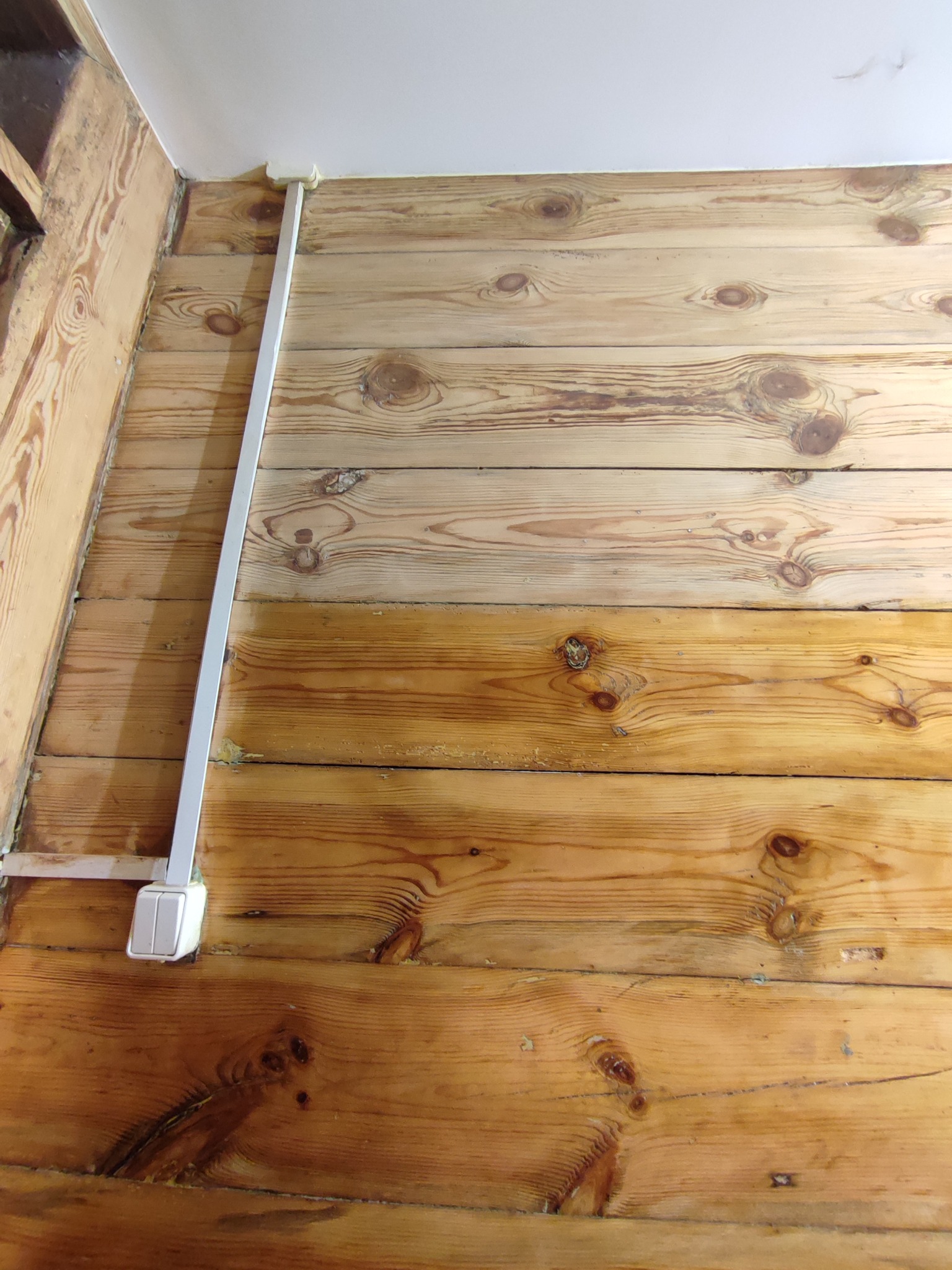 Ściana wyłożona boazerią z widocznym kanałem kablowym i gniazdkiem elektrycznym, drewno w dwóch odcieniach. Część ściany pomalowana na jaśniejszy kolor.