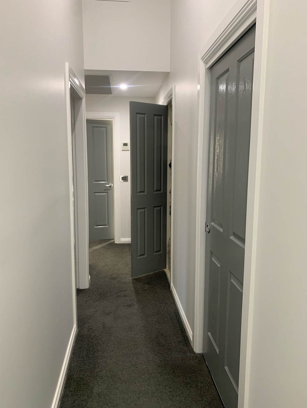 Korytarz po remoncie z szarymi ścianami i drzwiami, otwarte drzwi w głębi ukazują kolejne pomieszczenie, widoczna faktura świeżo pomalowanych ścian.