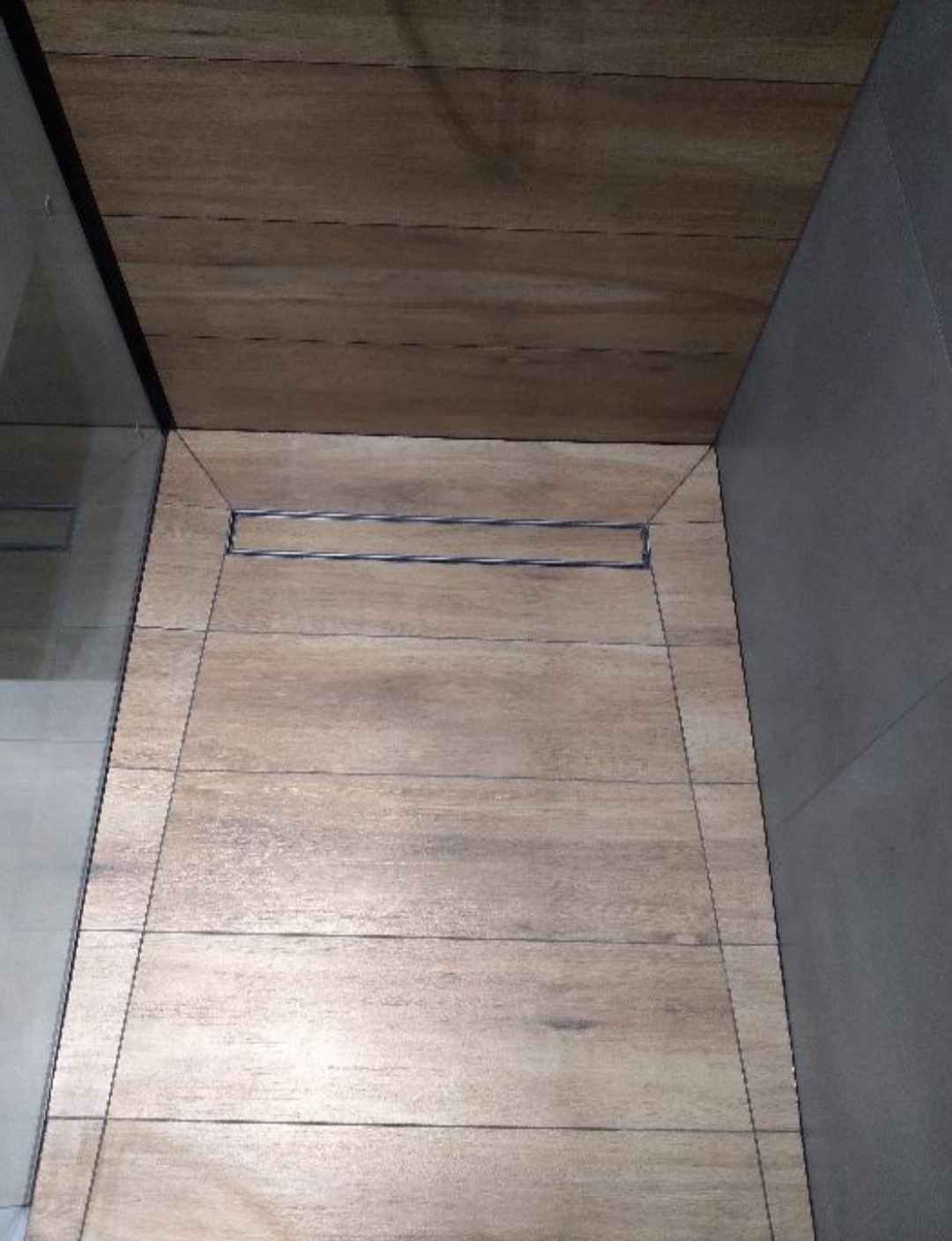 Ukończona łazienka z drewnopodobnymi płytkami na podłodze i suficie, z odpływem liniowym pod kabiną prysznicową, widok z góry.