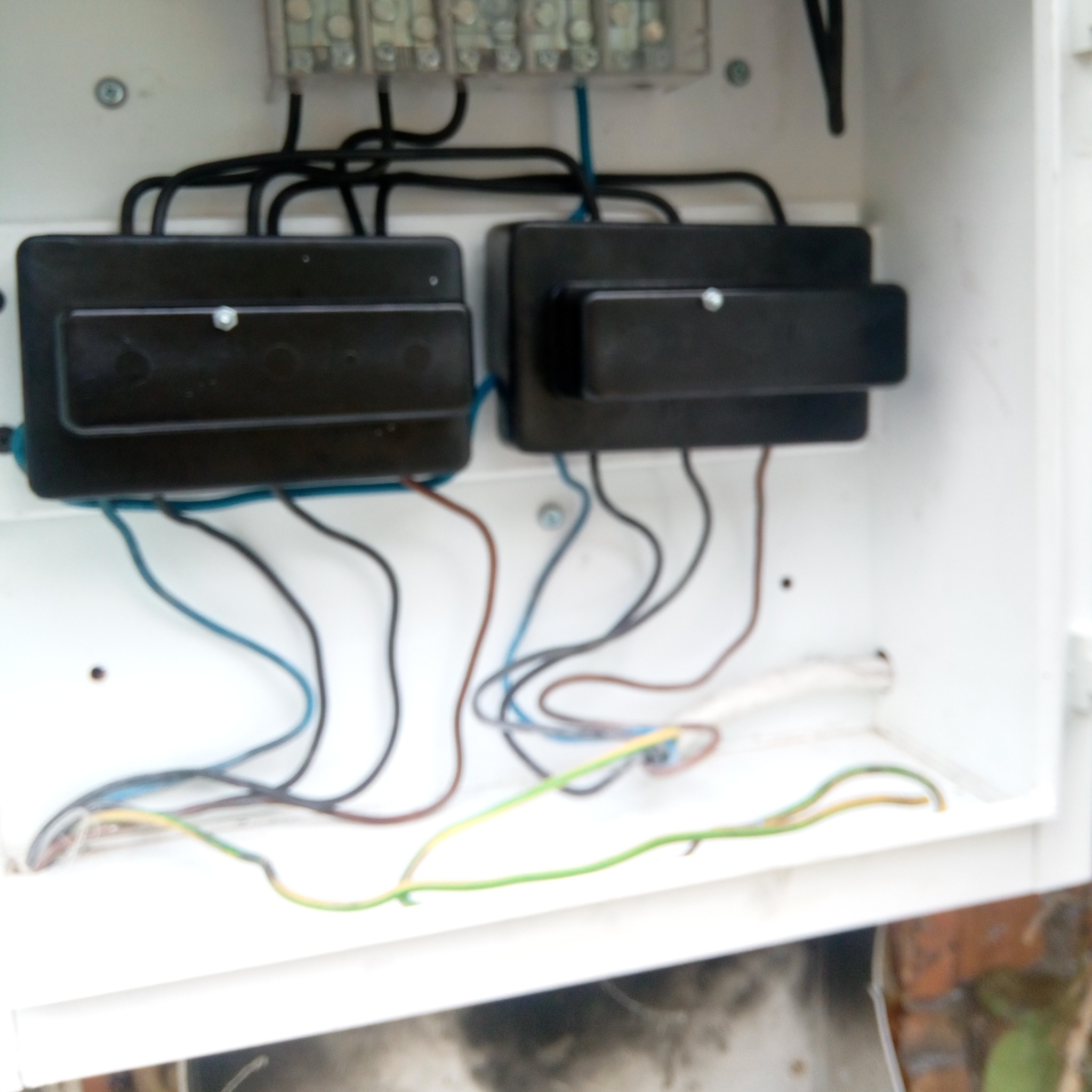 Otwarta, biała skrzynka rozdzielcza z dwoma czarnymi modułami zabezpieczeń, widoczne przewody w różnych kolorach podłączone do listwy zaciskowej na górze.