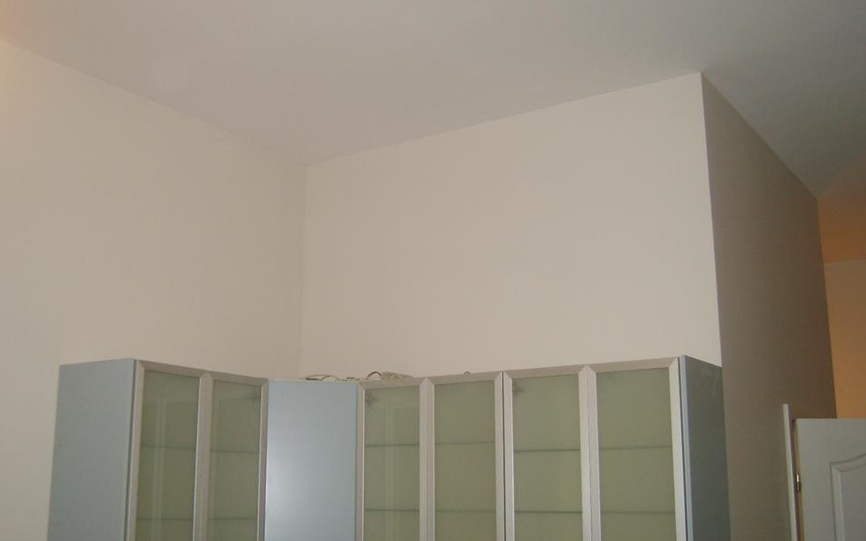 Świeżo pomalowane, jasne ściany i sufit w rogu pomieszczenia nad szafkami z mlecznym szkłem.