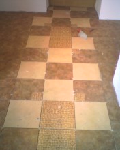 Układanie kwadratowej mozaiki podłogowej w szachownicę, widoczny fragment kleju, niedokończony etap prac.